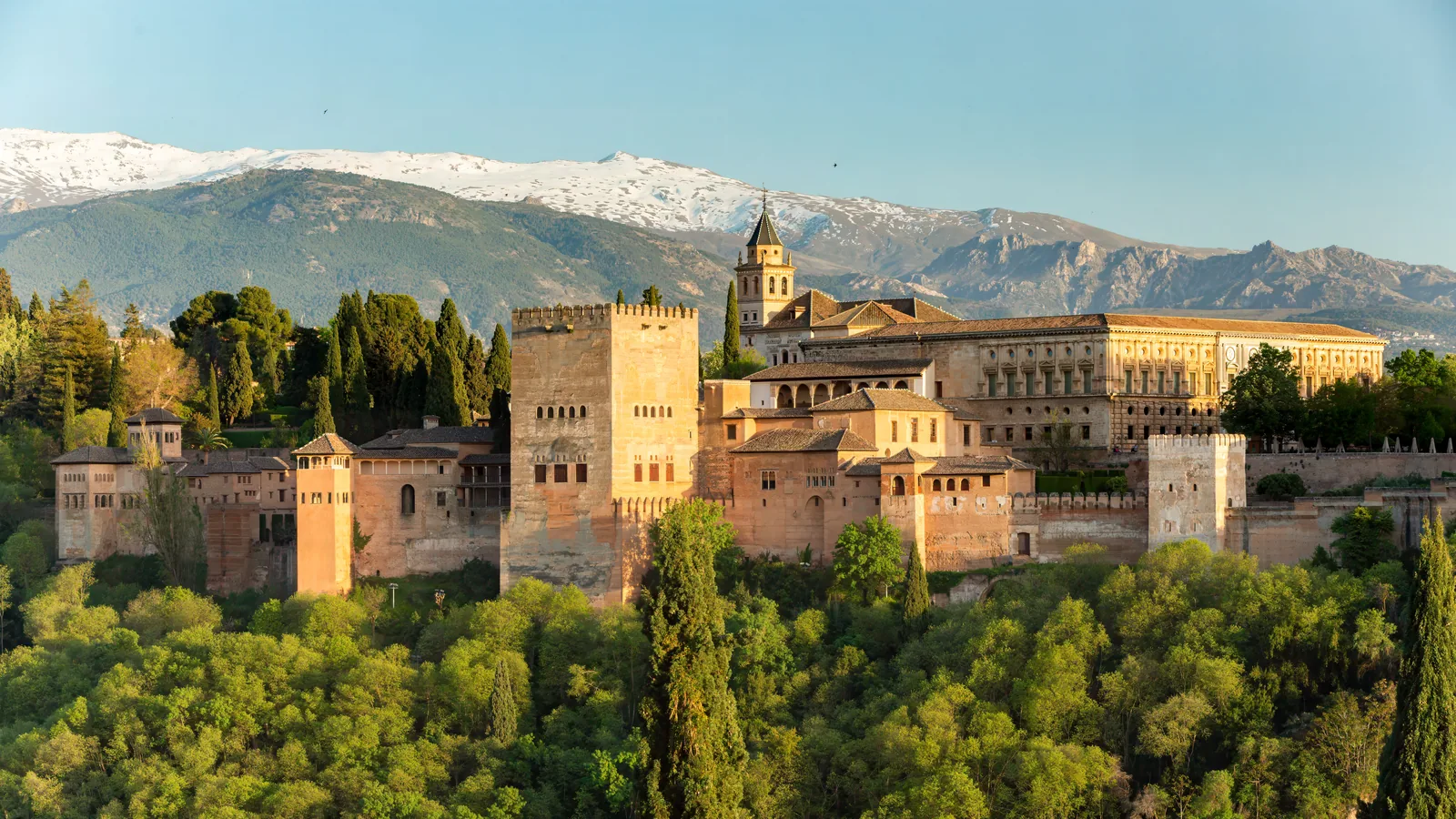 The Alhambra in warm low light seen from the Mirador de San Nicolás, with the snow-topped Sierra Nevada behind it