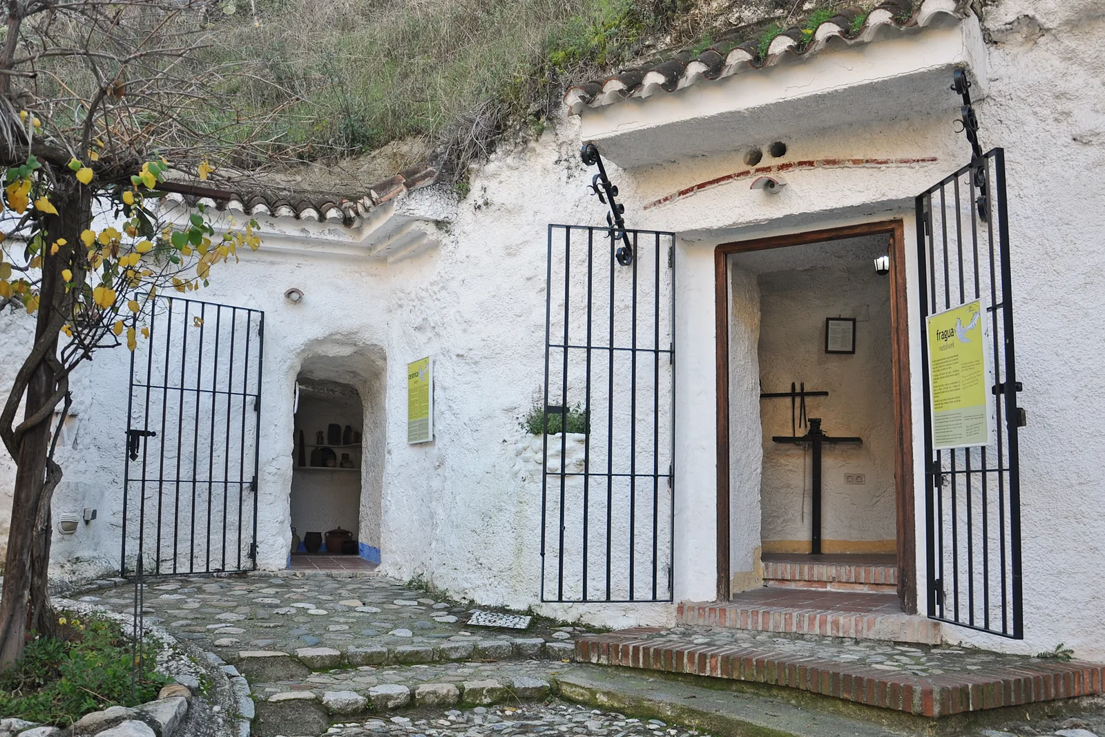 The whitewashed front of a cave building at the Sacromonte Caves Museum, with a tiled roof edge, iron gates and a lemon tree