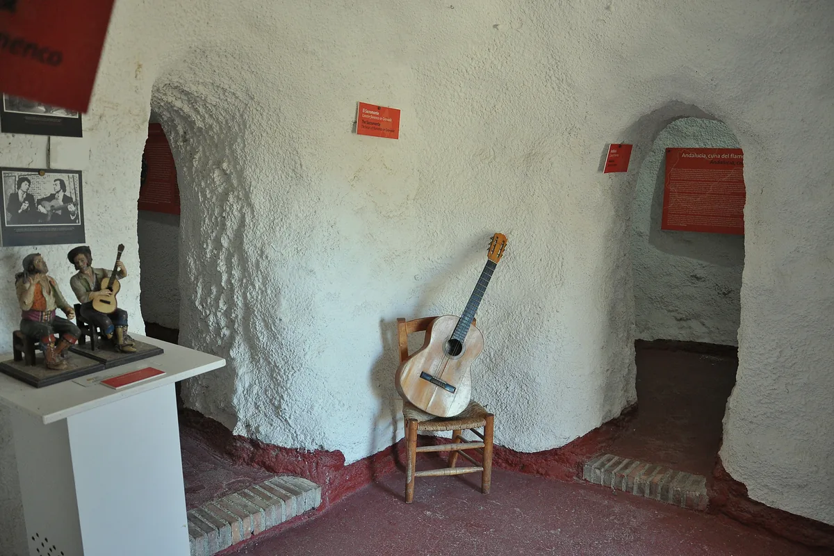 A guitar on a wooden chair in a rounded whitewashed cave room at the Sacromonte Caves Museum